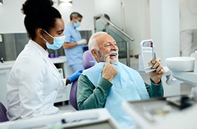 Senior dental patient holding mirror, looking at his teeth