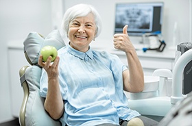 Older dental patient holding apple and smiling