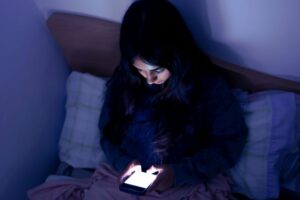 Woman sitting up in bed, using her phone at night